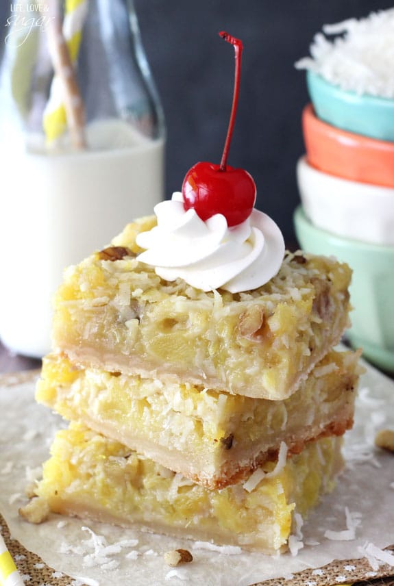 Pineapple Coconut Bars stacked with whipped cream and a cherry on top