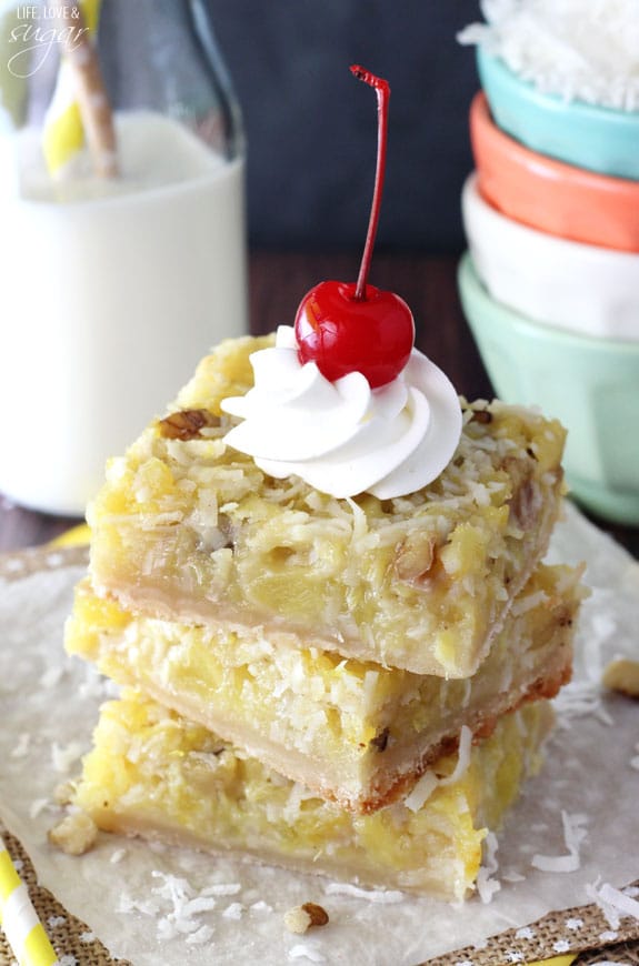 Pineapple Coconut Bars stacked on a napkin with whipped cream and a cherry on top