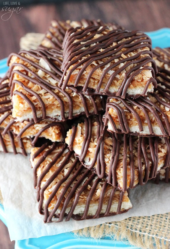 A close-up shot of chocolate caramel coconut dessert bars piled onto a cake stand lined with parchment paper