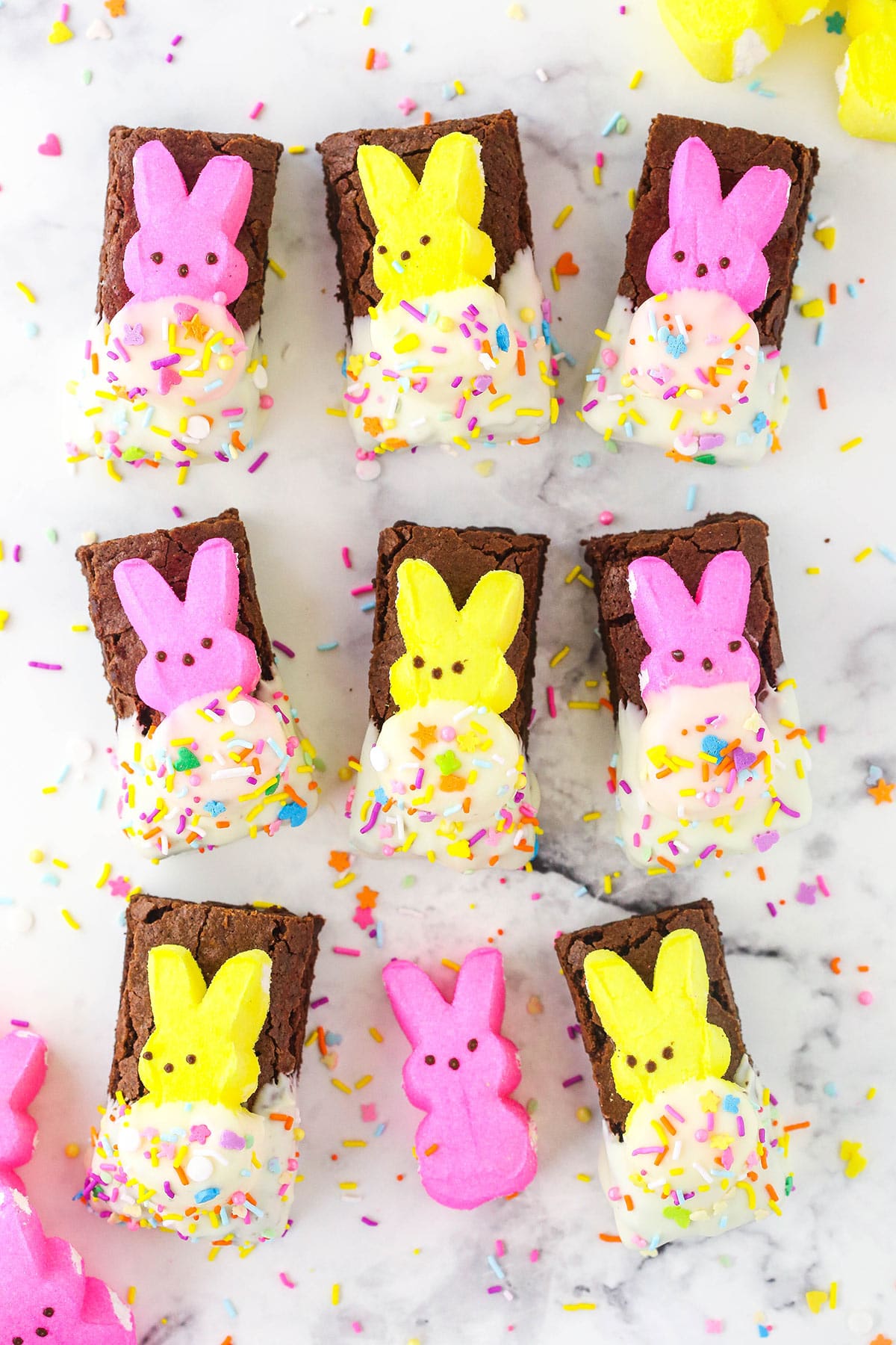 brownies with peeps on top sitting on marble table with sprinkles all around
