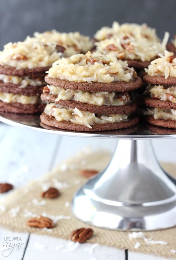 Multiple stacks of German Chocolate Cookies with layers of coconut pecan frosting on a silver cake stand