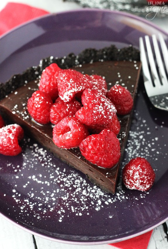 Close up top view of a slice of Nutella tart topped with fresh raspberries and powdered sugar on a purple plate