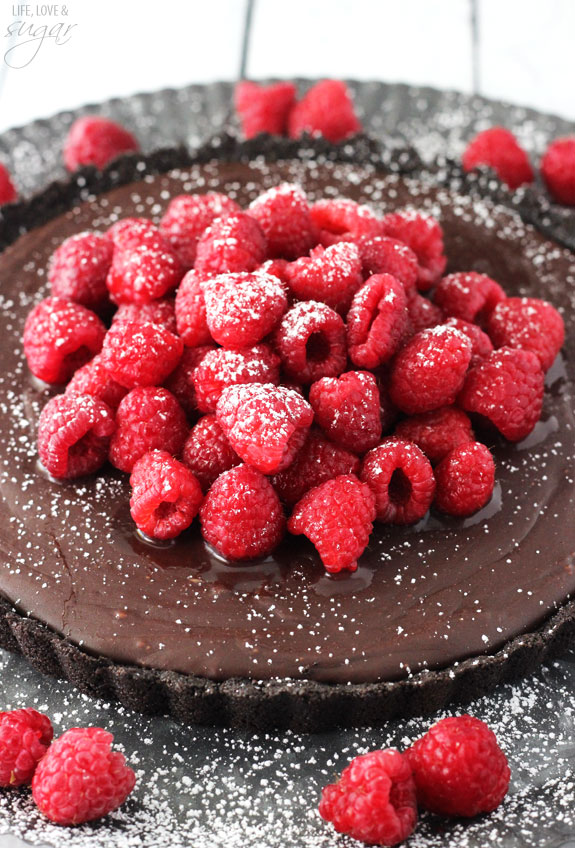 A homemade Nutella chocolate tart topped with sugar coated raspberries and surrounded by more raspberries