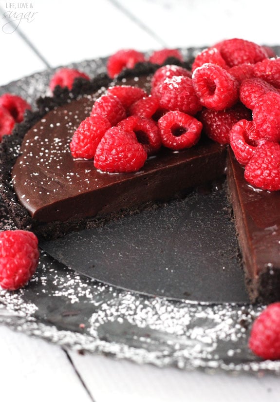 A chocolate Nutella tart topped with raspberries is missing a slice on a dark plate