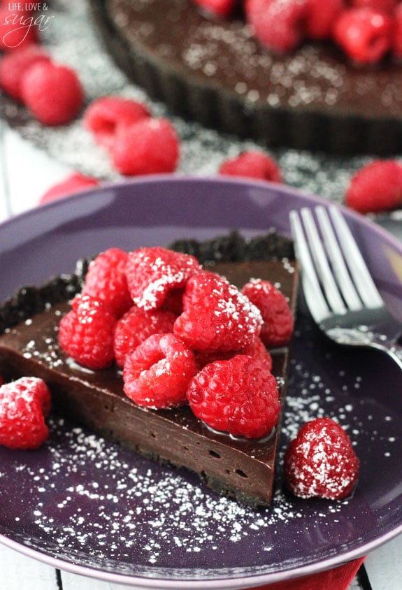 A slice of Nutella Tart on a purple plate topped with raspberries and sugar