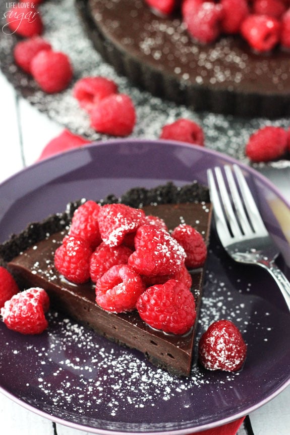 A slice of Nutella Raspberry Tart on a purple plate with a fork and fresh raspberries