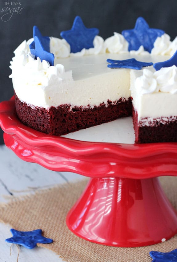 Red Velvet Blondie Cheesecake topped with blue stars on a red cake stand with a slice removed
