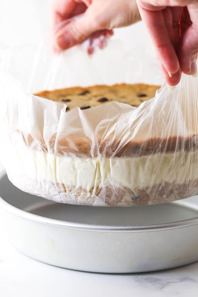 Lifting a chocolate chip ice cream cookie cake out of the pan with parchment paper