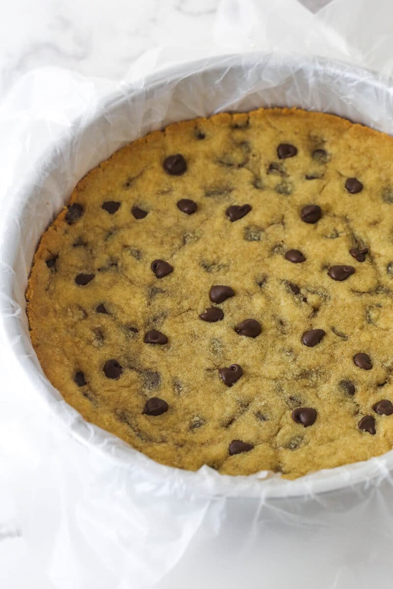 A chocolate chip cookie in a round pan with parchment paper