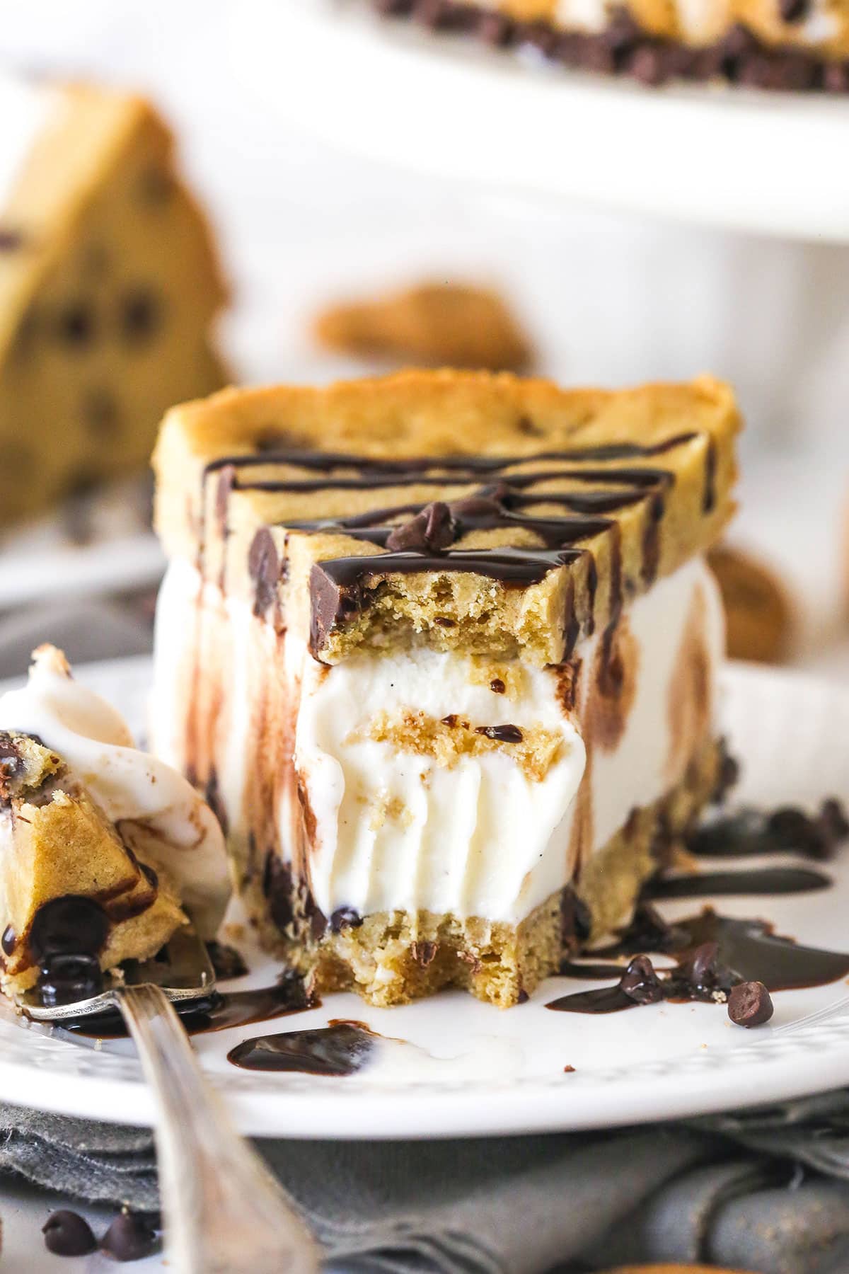 Front view of a chocolate chip cookie ice cream cake slice on a plate with a bite on the fork next to it