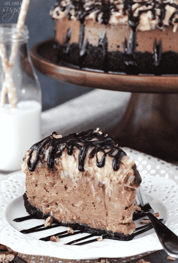 German Chocolate Cheesecake slice on a plate in front of a whole cake on a wooden stand