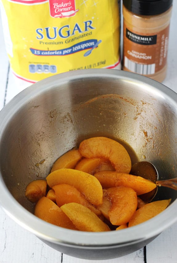 Sliced peaches in a bowl next to cinnamon and sugar