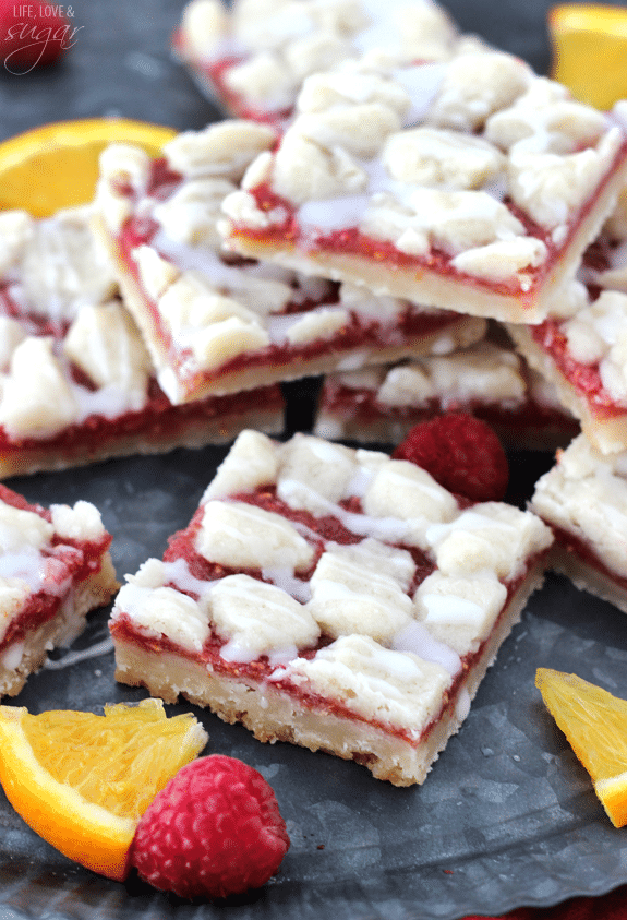 Raspberry Orange Shortbread Bars stacked together with scattered fruit around