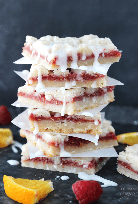 Raspberry Orange Shortbread Bars stacked between squares of parchment paper