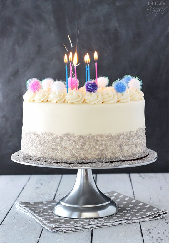 Sparkly Pom Pom Cake topped with candles on a silver cake stand 