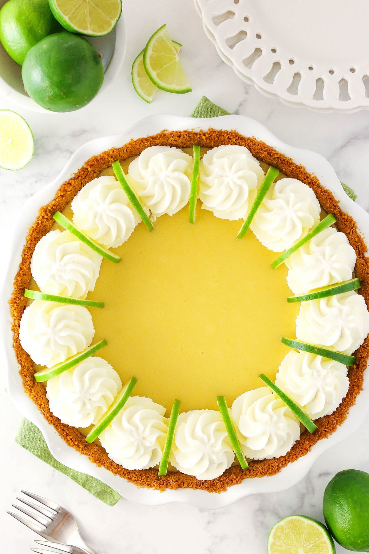 A homemade key lime pie inside of a pie dish with a green kitchen towel underneath the dish and swirls of whipped cream on top of the pie filling