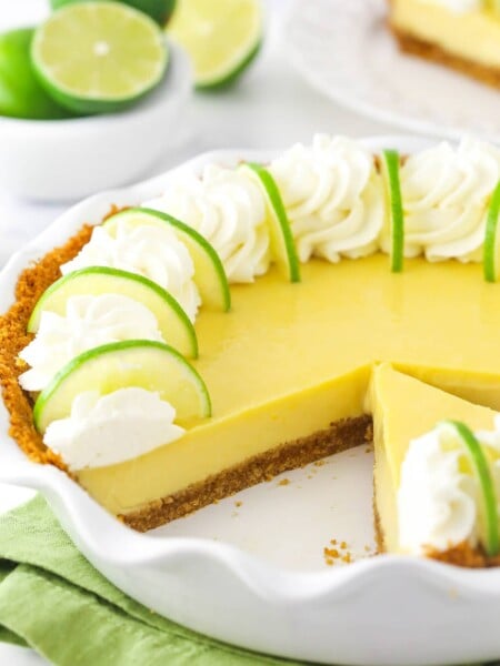 A homemade key lime pie inside of a pie dish with one slice missing and a bowl of fresh limes in the background