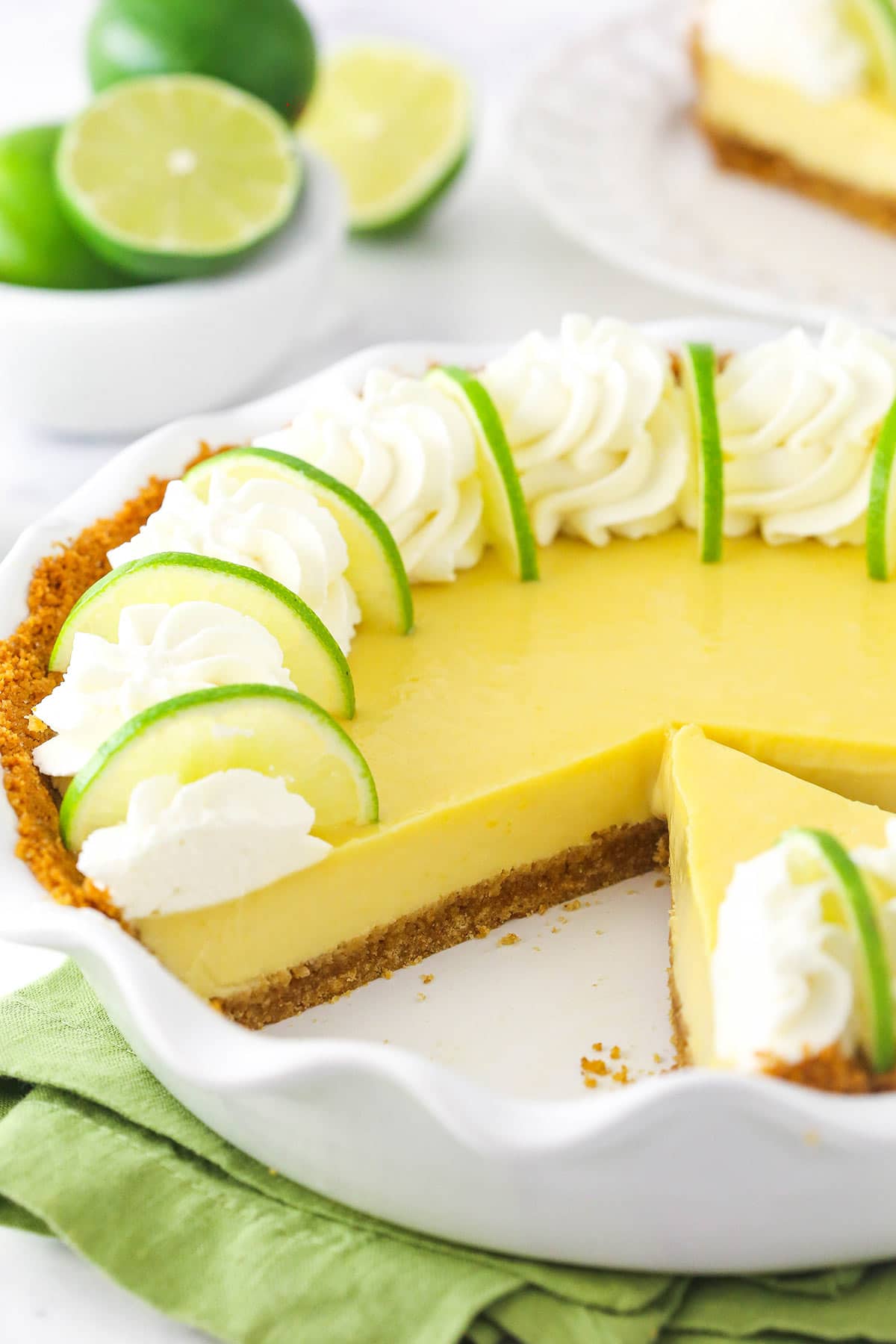 A homemade key lime pie inside of a pie dish with one slice missing and a bowl of fresh limes in the background