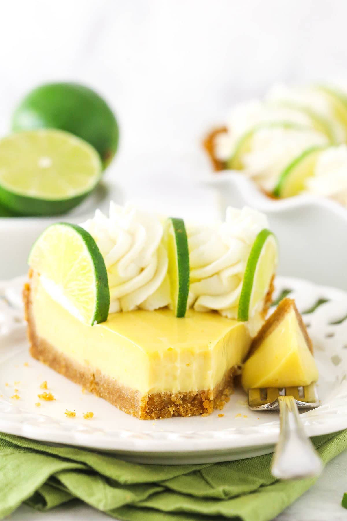 A slice of key lime pie on a plate with one bite on a metal fork beside the slice