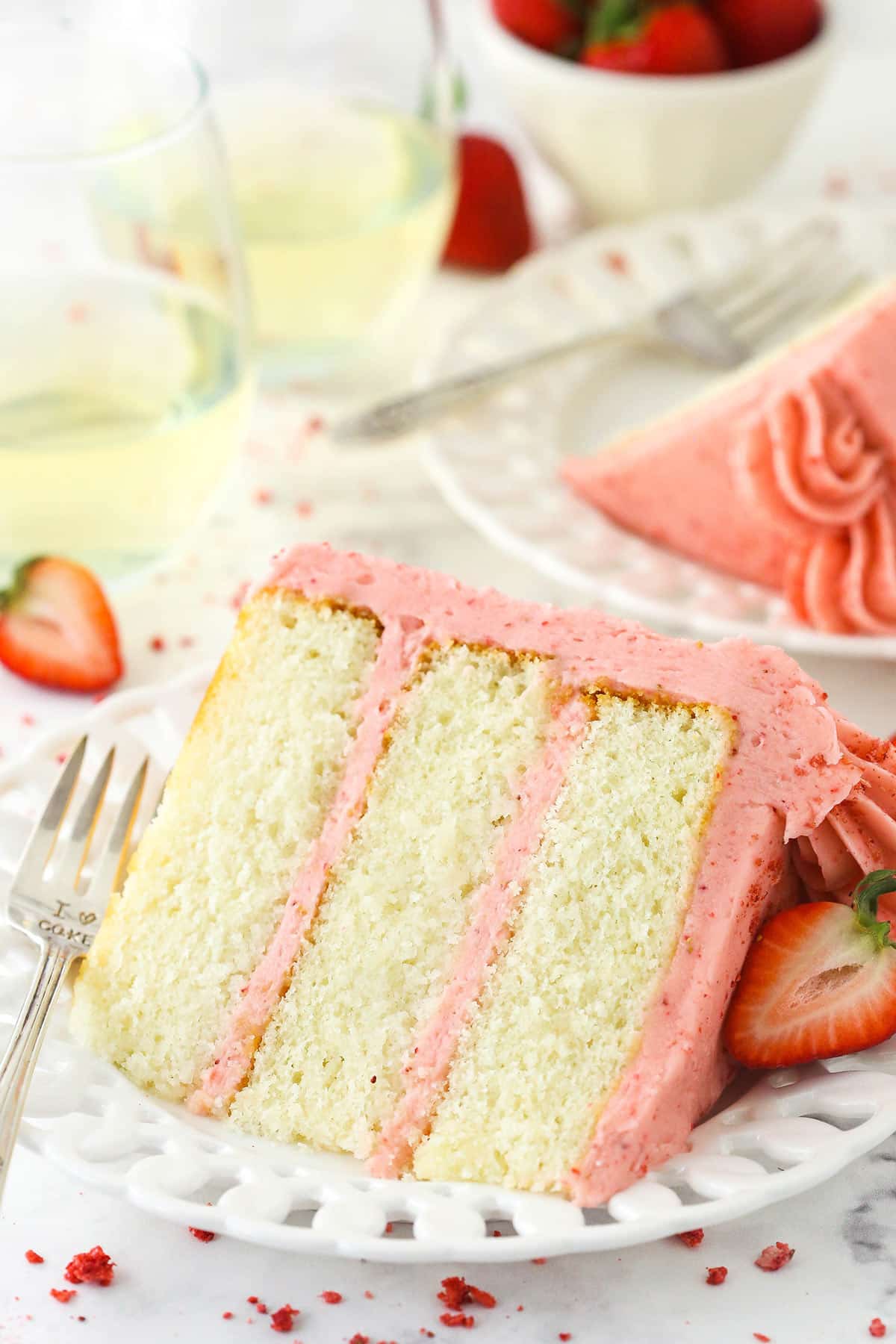 a slice of strawberry moscato cake on a white plate with strawberries and wine in the background