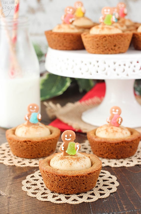 Gingerbread Cheesecake Cookie Cups topped with mini gingerbread cookies in front of a white cake stand with more cookie cups