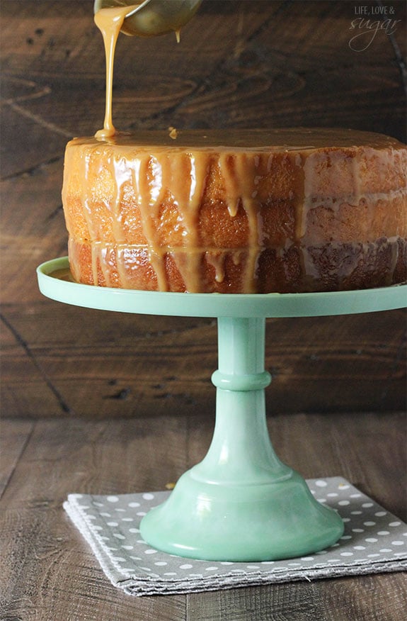 Caramel sauce being poured onto a cake on a stand