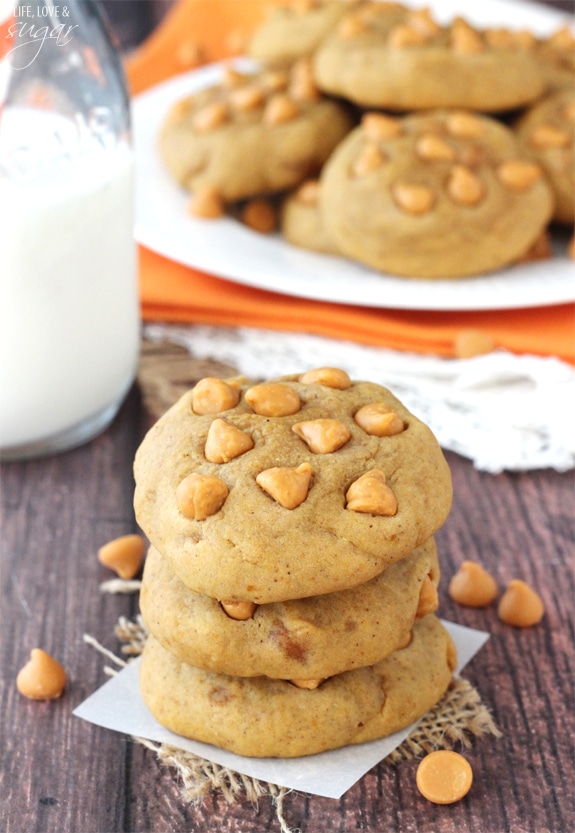 Pumpkin Butterscotch Chip Cookies stacked on a square of parchment in front of a jar of milk and a plate of cookies