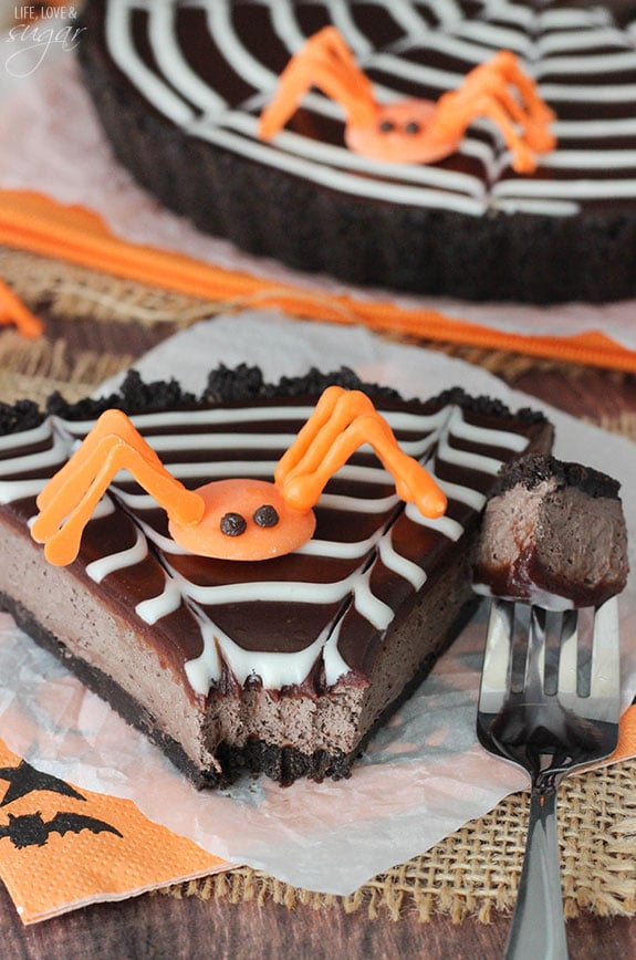 Spiderweb Chocolate Tart slice topped with an orange candy spider on a napkin with a bite on a fork and 