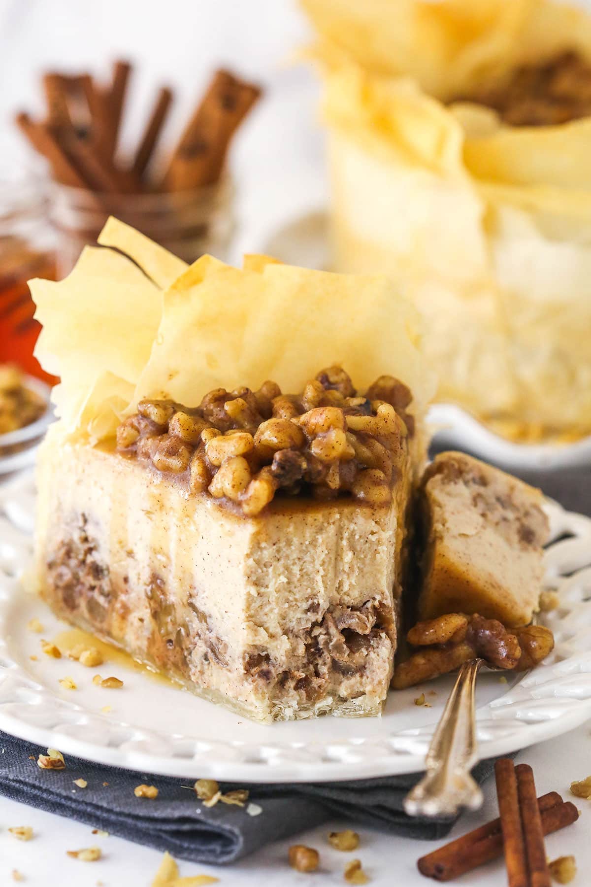 With a phyllo dough crust, creamy cheesecake filling, and honey walnut topping, Baklava Cheesecake is a fun twist on the traditional dessert. A slice of baklava cheesecake on a plate with a bite on a fork next to it