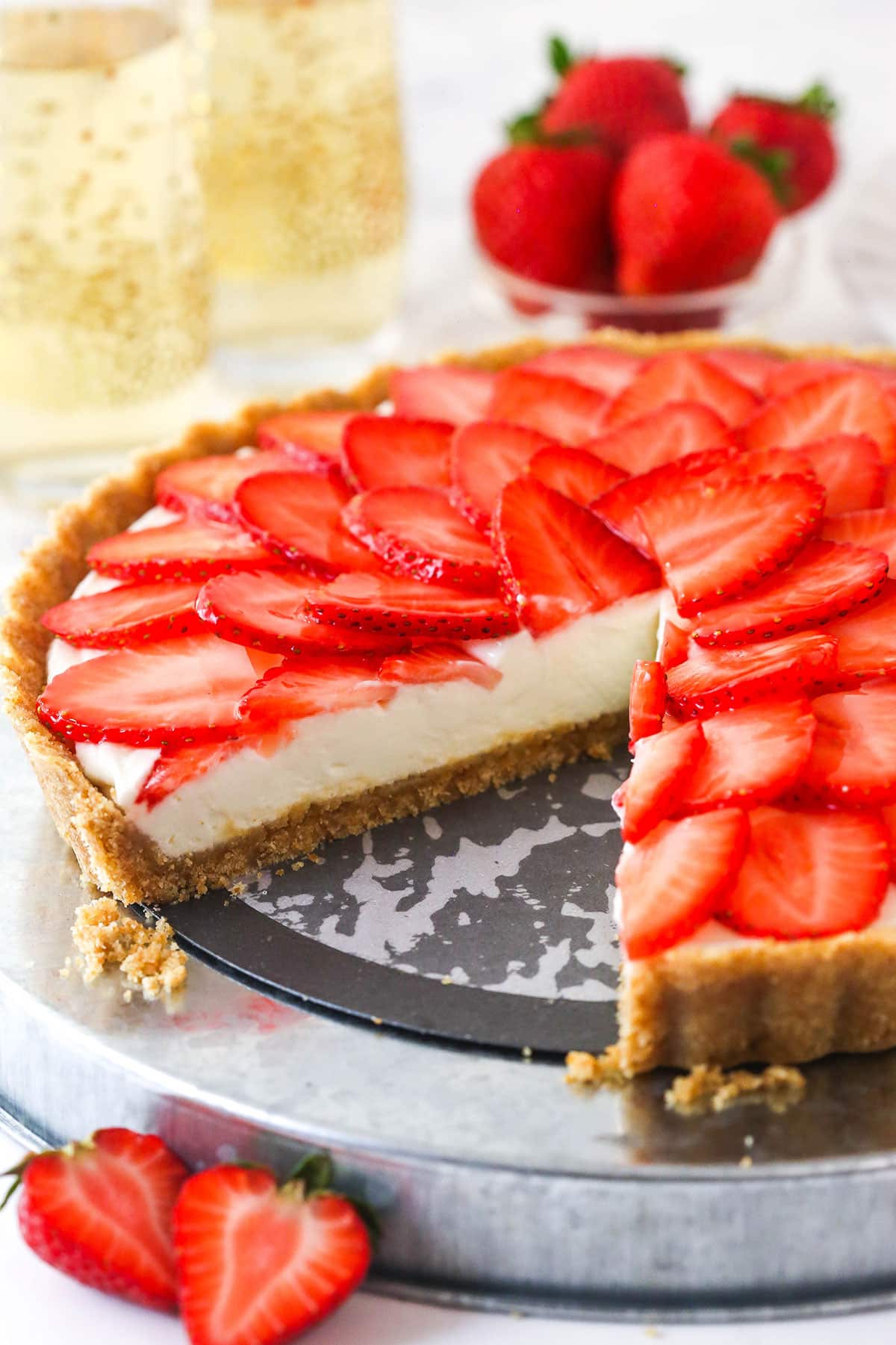 A wafer crust surrounds a creamy champagne mascarpone tart filling, topped with juicy strawberry slices, to create the best strawberry tart! strawberry champagne tart on silver platter with slice cut out