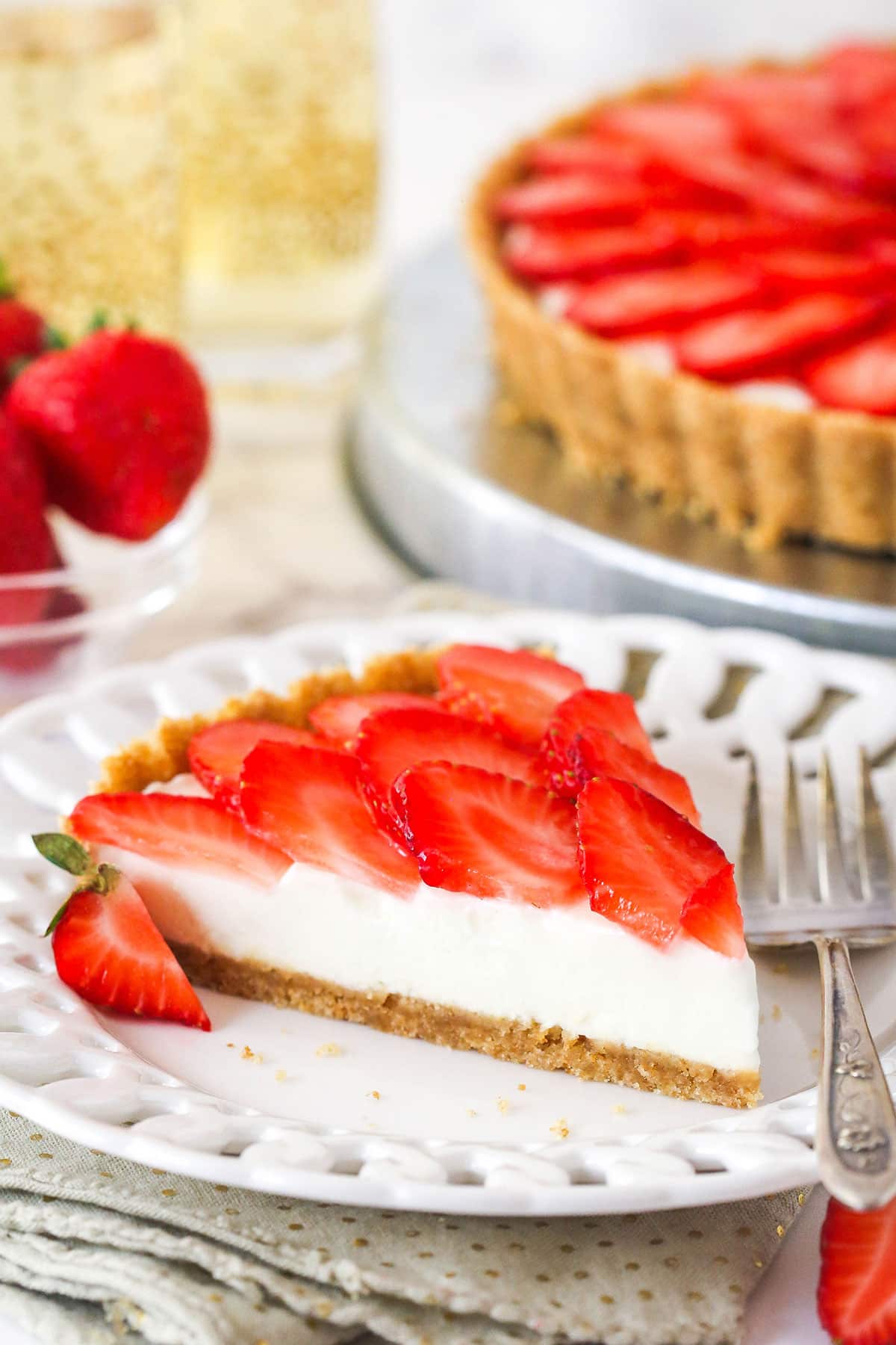 A wafer crust surrounds a creamy champagne mascarpone tart filling, topped with juicy strawberry slices, to create the best strawberry tart! slice of strawberry champagne tart on a white plate