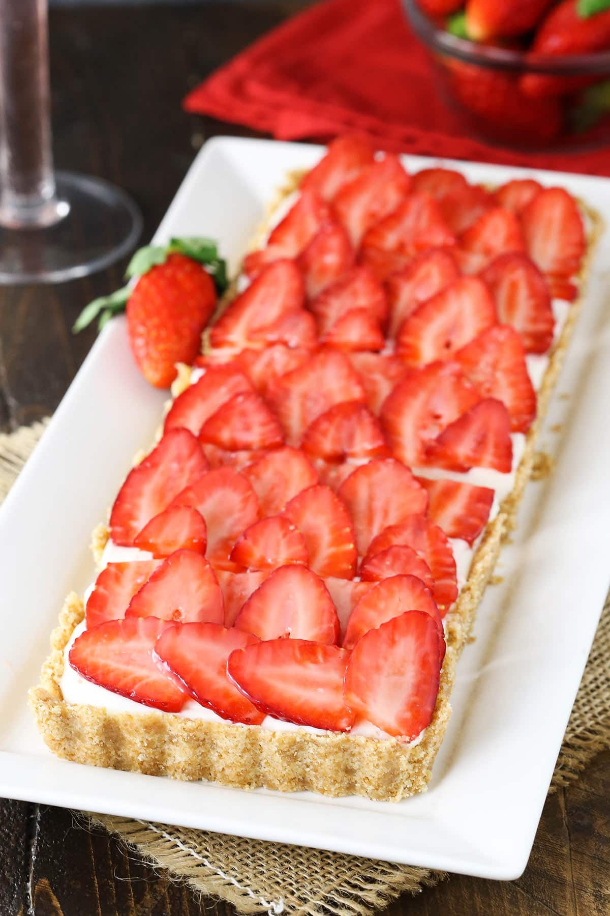 A strawberry champagne tart on a white platter with a fresh strawberry beside it.