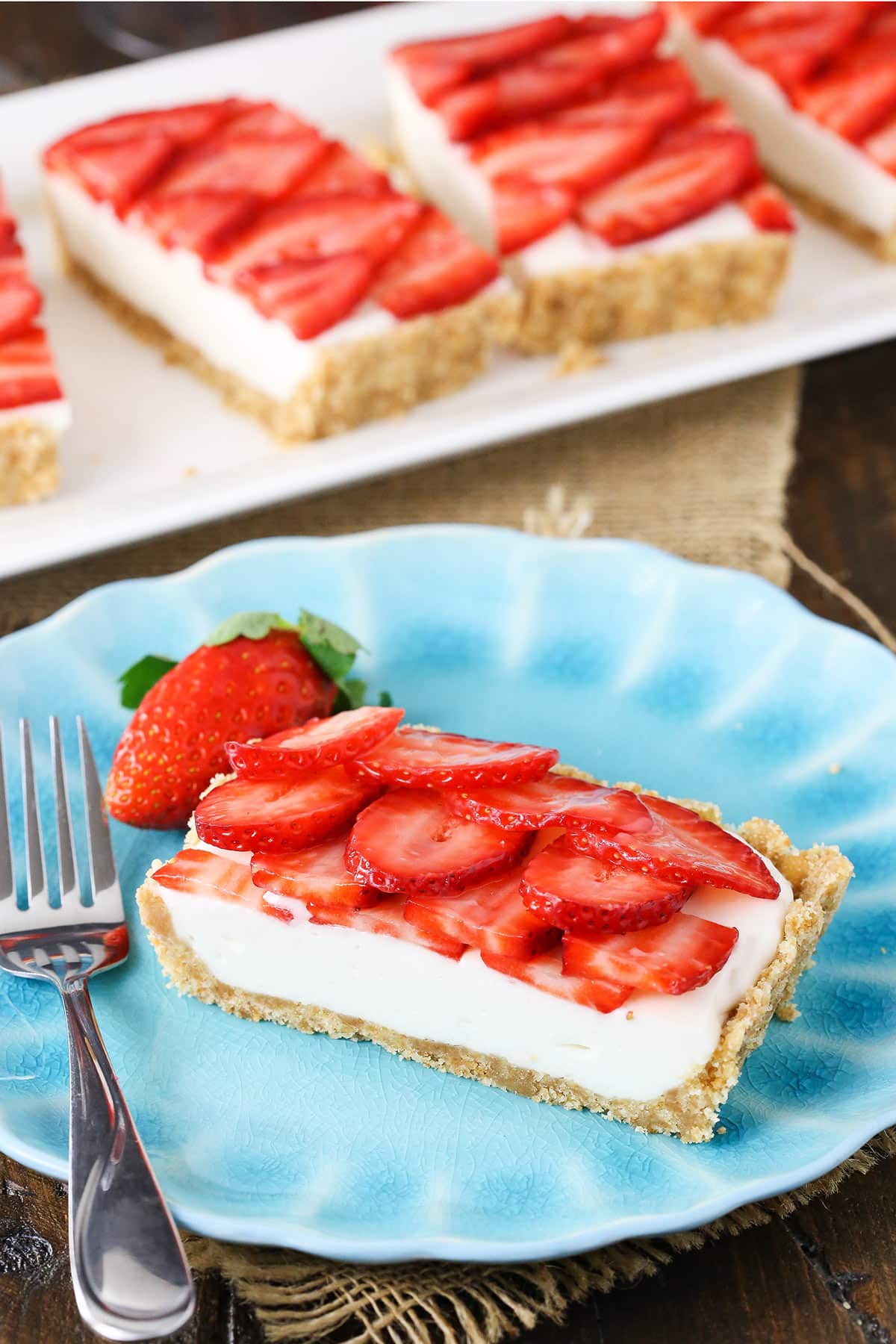 A blue plate holding a slice of champagne tart, a fork, and a fresh strawberry.