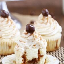 A frosted tiramisu cupcake with a bite missing, showing the espresso-soaked interior filled with mascarpone cream.