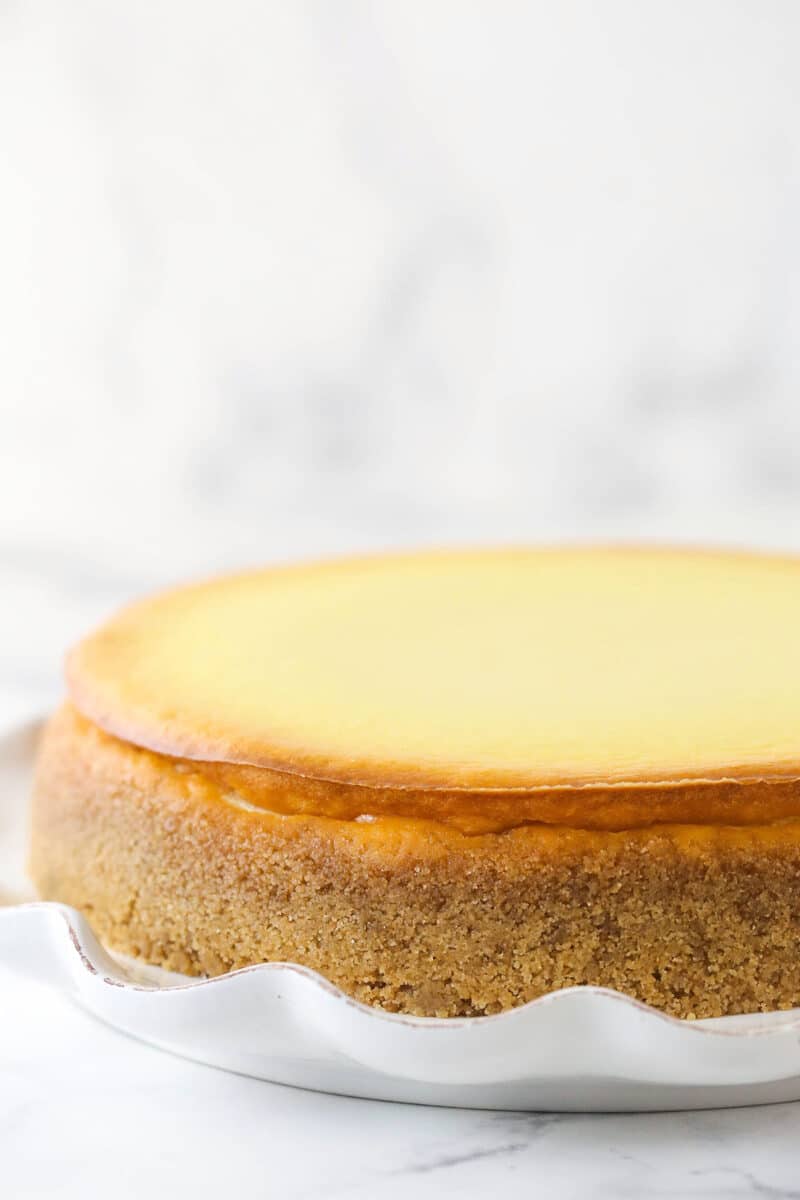 A cheesecake with a pan of water underneath on a serving platter