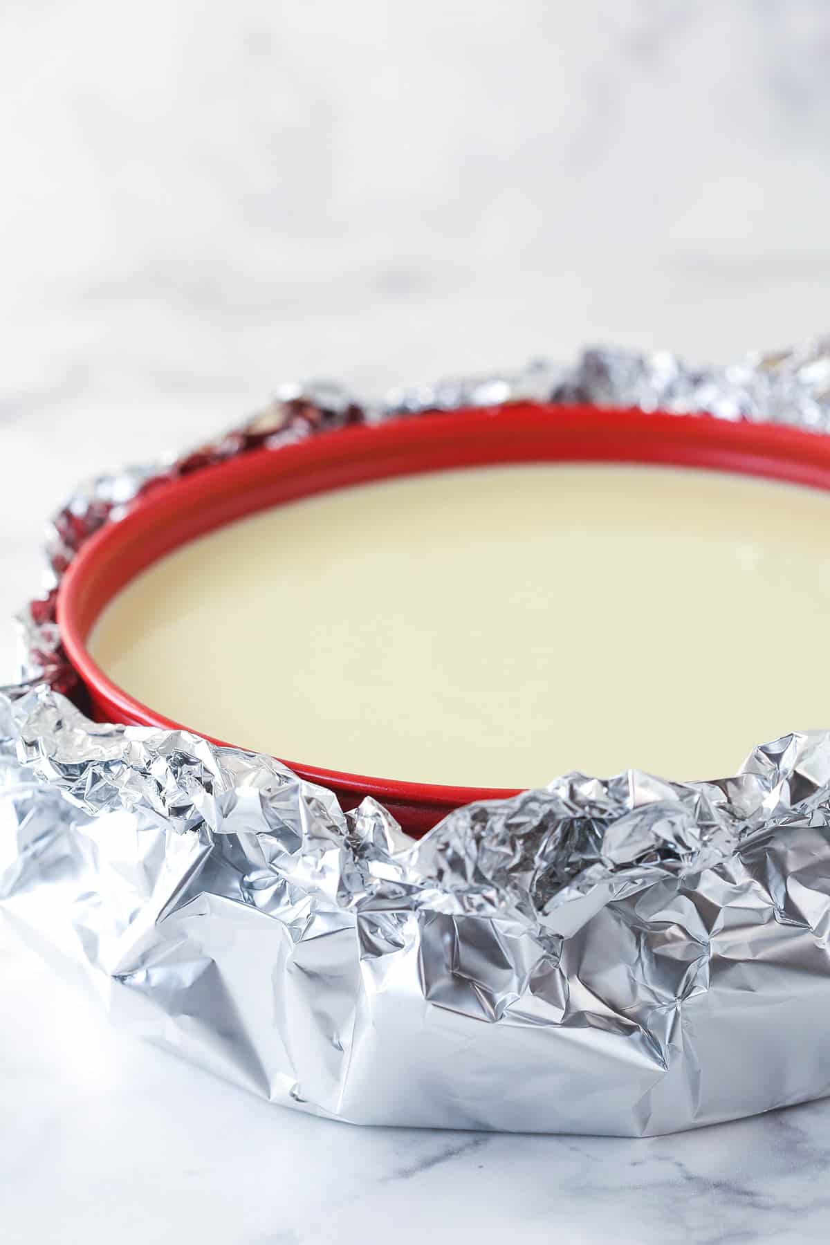 a cheesecake in a springform pan wrapped in aluminum foil for a water bath