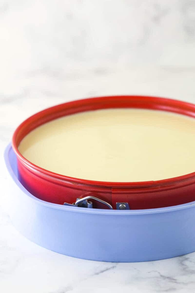 a cheesecake in a springform pan placed in a purple silicone pan for a water bath