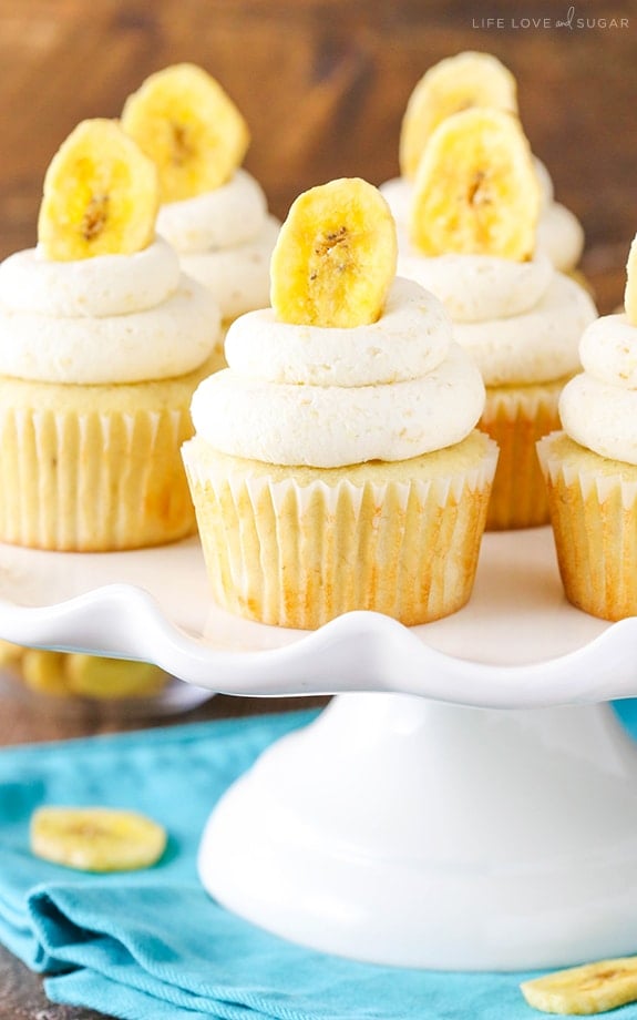 A bunch of Banana Cupcakes on top of a cake stand and blue cloth