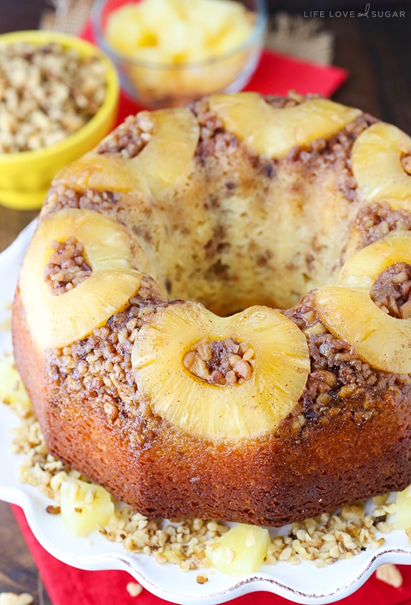 Pineapple Walnut Upside Down Bundt Cake on a white cake plate with nuts sprinkled around it