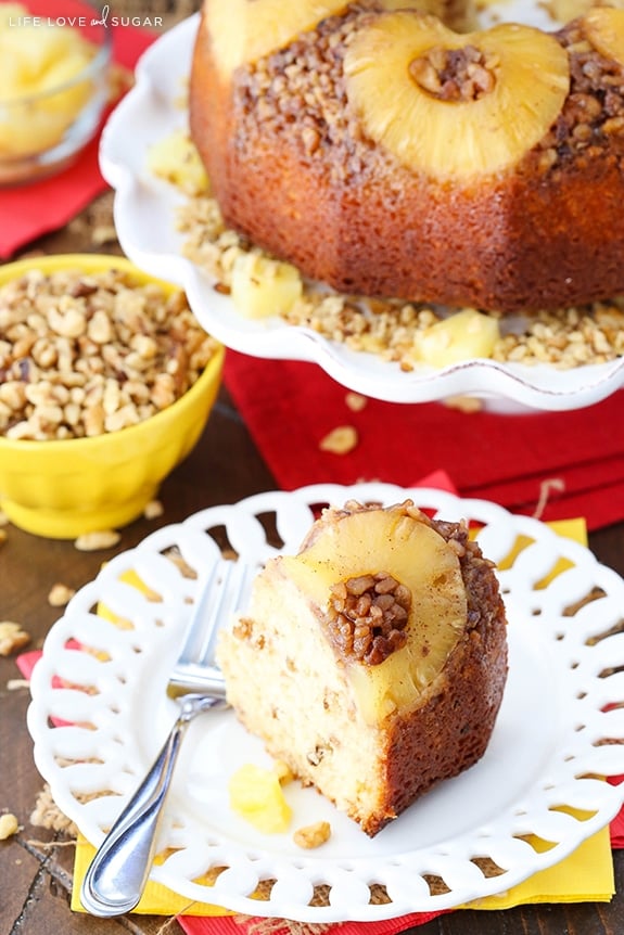 A slice of cake with a pineapple and nuts on top sits on a white plate with a fork