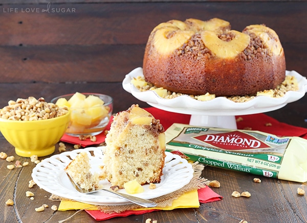 A slice of cake is on a white plate with a fork and a whole Pineapple Walnut Upside Down Bundt Cake is behind it 