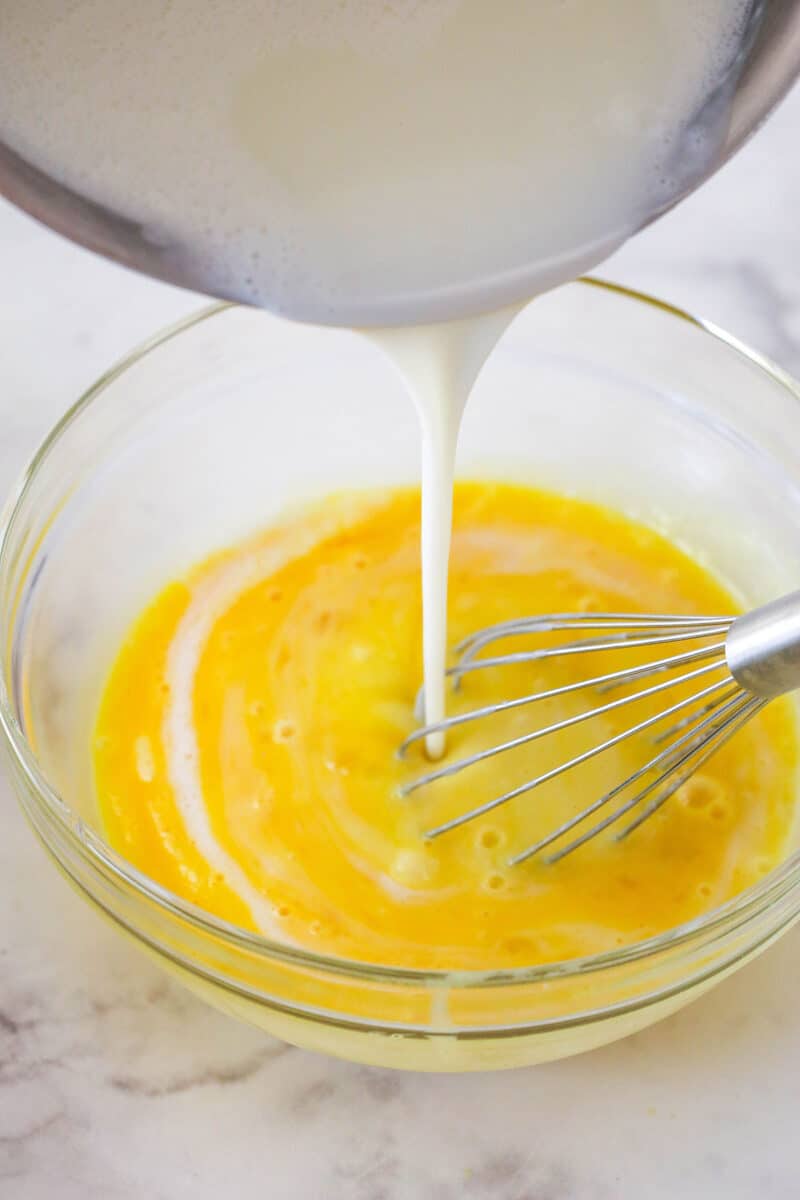 Pouring warm milk into whisked eggs