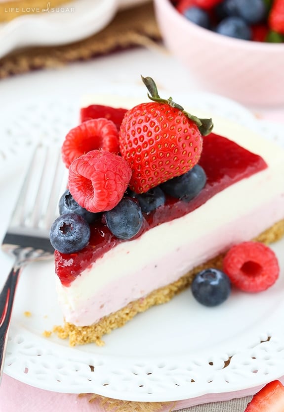 Close up of a slice of cheesecake topped with blueberries, raspberries and a strawberry on a plate