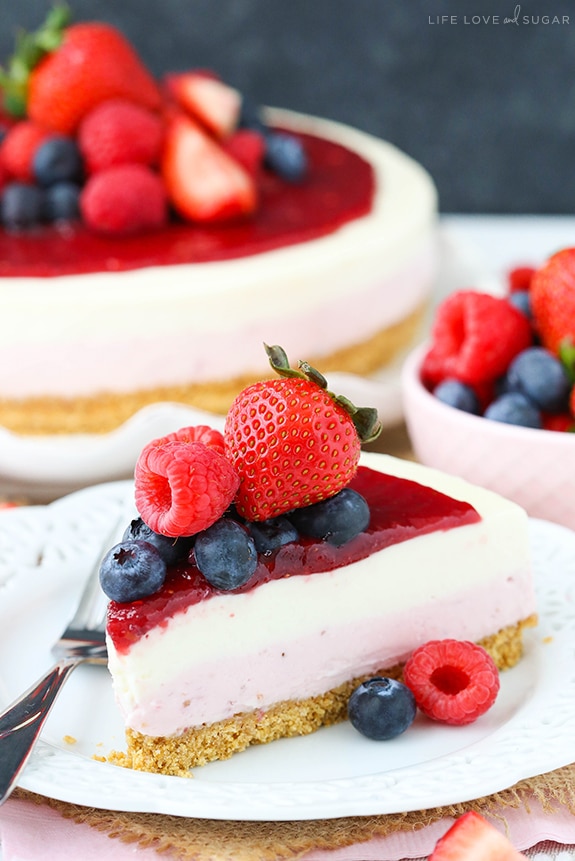 A slice of Berry Vanilla Cheesecake showing a layer of berry and vanilla filling, a graham cracker crust and a berry topping