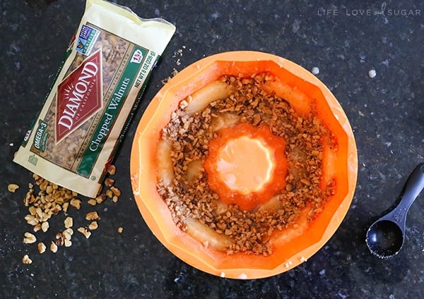 An orange bundt cake pan with nuts inside sits next to a bag of chopped walnuts