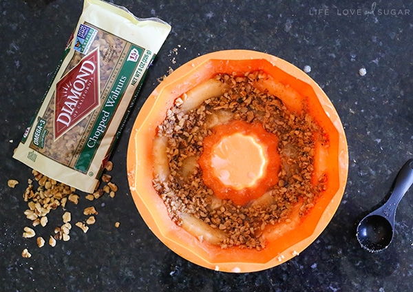 An orange bundt cake pan with nuts inside sits next to a bag of chopped walnuts