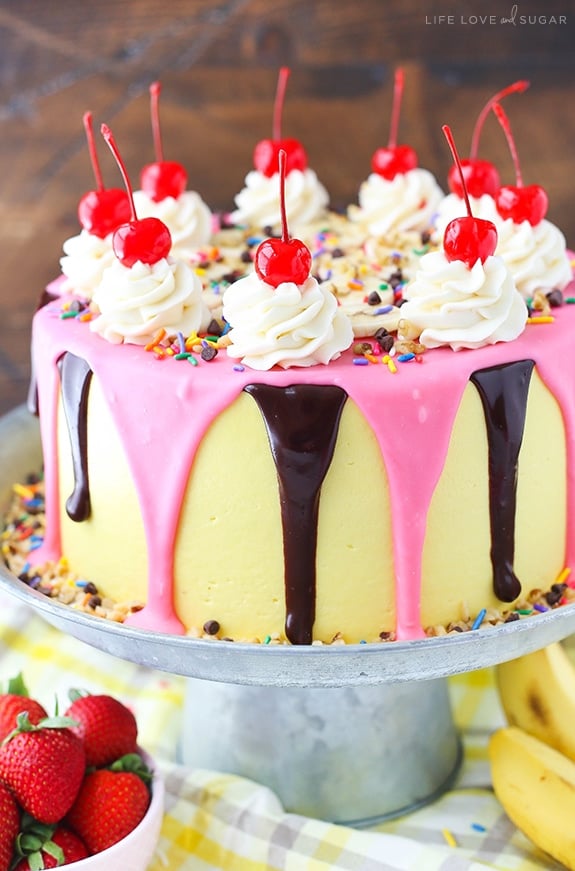 Banana Split Layer Cake - layers of moist banana cake with chocolate and strawberry buttercream filling, sliced bananas and strawberries, nuts, sprinkles and chocolate ganache! Banana split cake heaven!