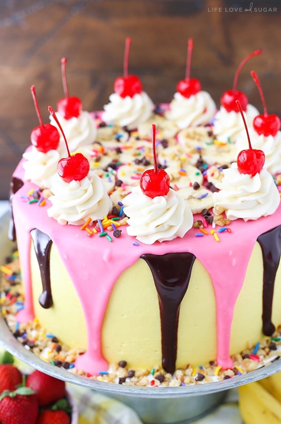 Banana Split Layer Cake - layers of moist banana cake with chocolate and strawberry buttercream filling, sliced bananas and strawberries, nuts, sprinkles and chocolate ganache! Banana split cake heaven!