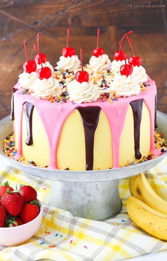 Banana Split Layer Cake - layers of moist banana cake with chocolate and strawberry buttercream filling, sliced bananas and strawberries, nuts, sprinkles and chocolate ganache! Banana split cake heaven!