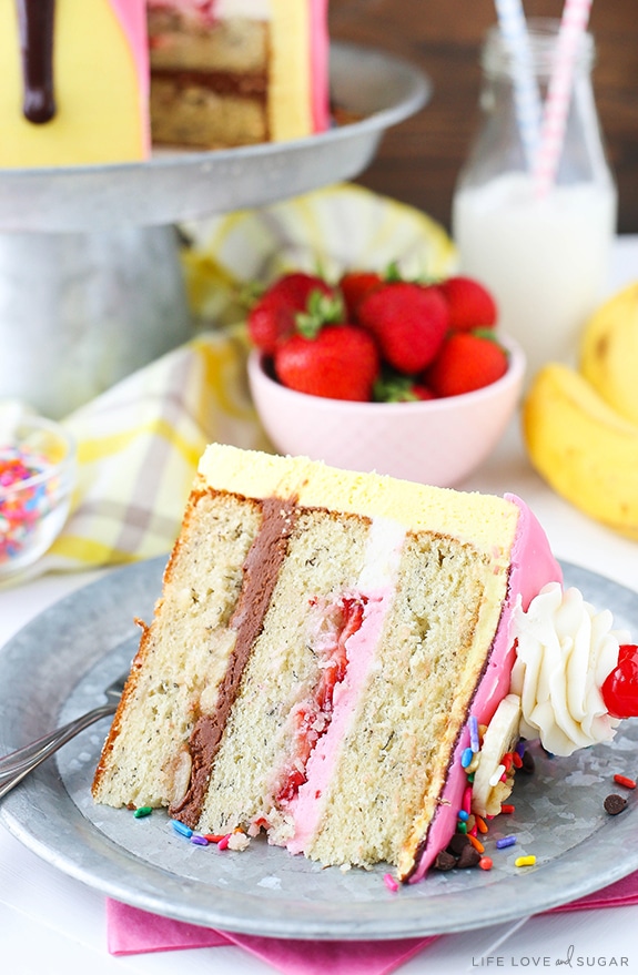 Banana Split Layer Cake - layers of moist banana cake with chocolate and strawberry buttercream filling, sliced bananas and strawberries, nuts, sprinkles and chocolate ganache! Banana split cake heaven!